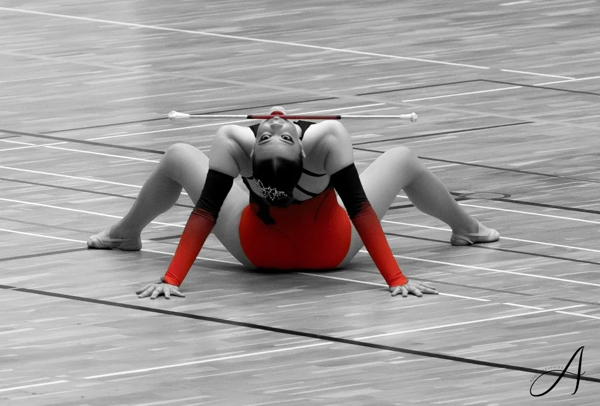 Atleta in gara seduta a terra a gambe aperte, il bastone in equilibrio sulla testa
